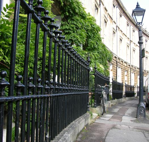 An image of black cast-iron traditional railings against a backdrop of greenery