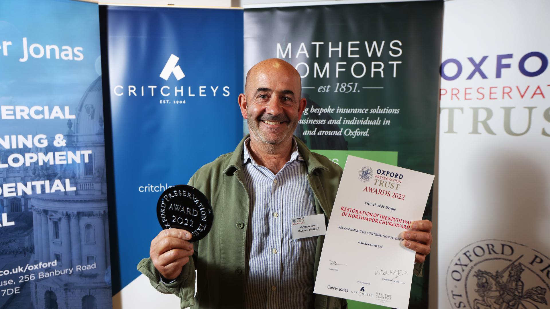 A man holding up an OPT awards plaque and certificate