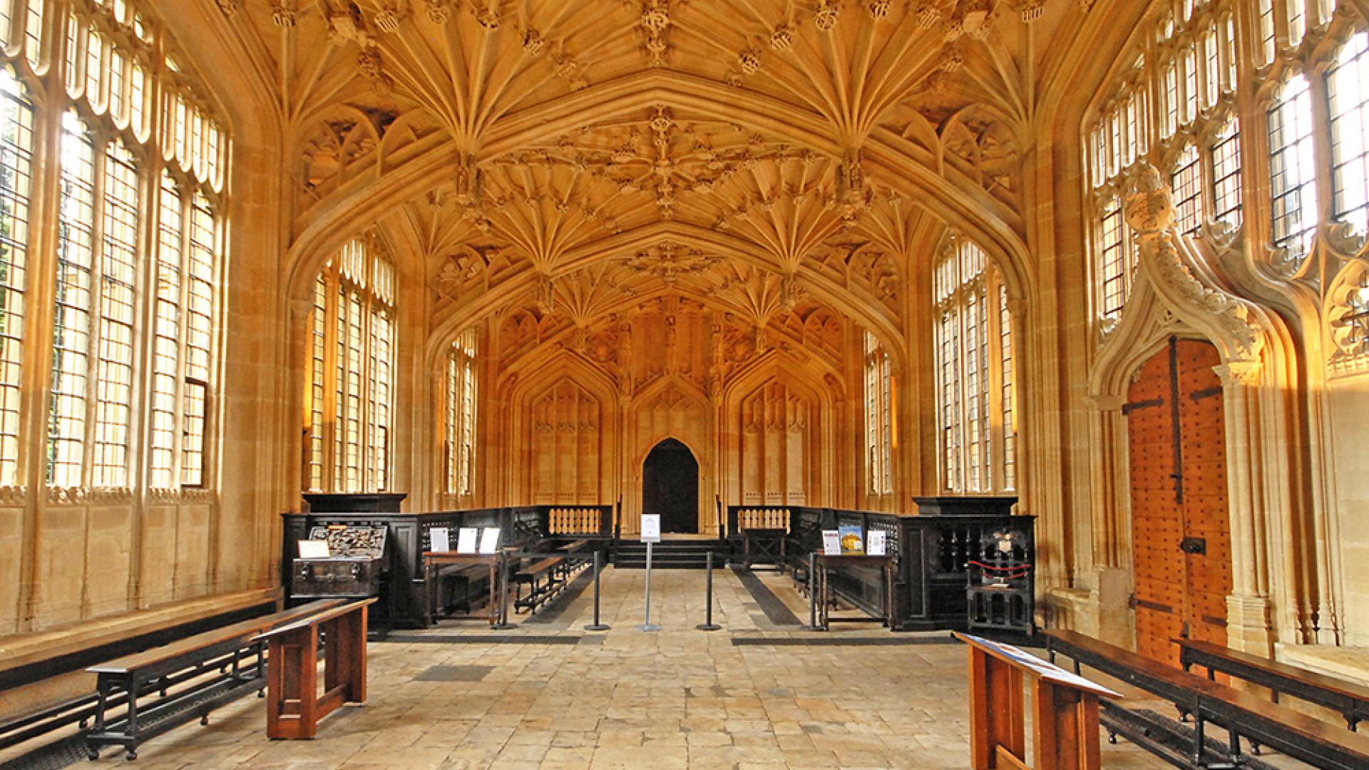 A room with an elaborate fan vaulted ceiling and wooden benches on either side.