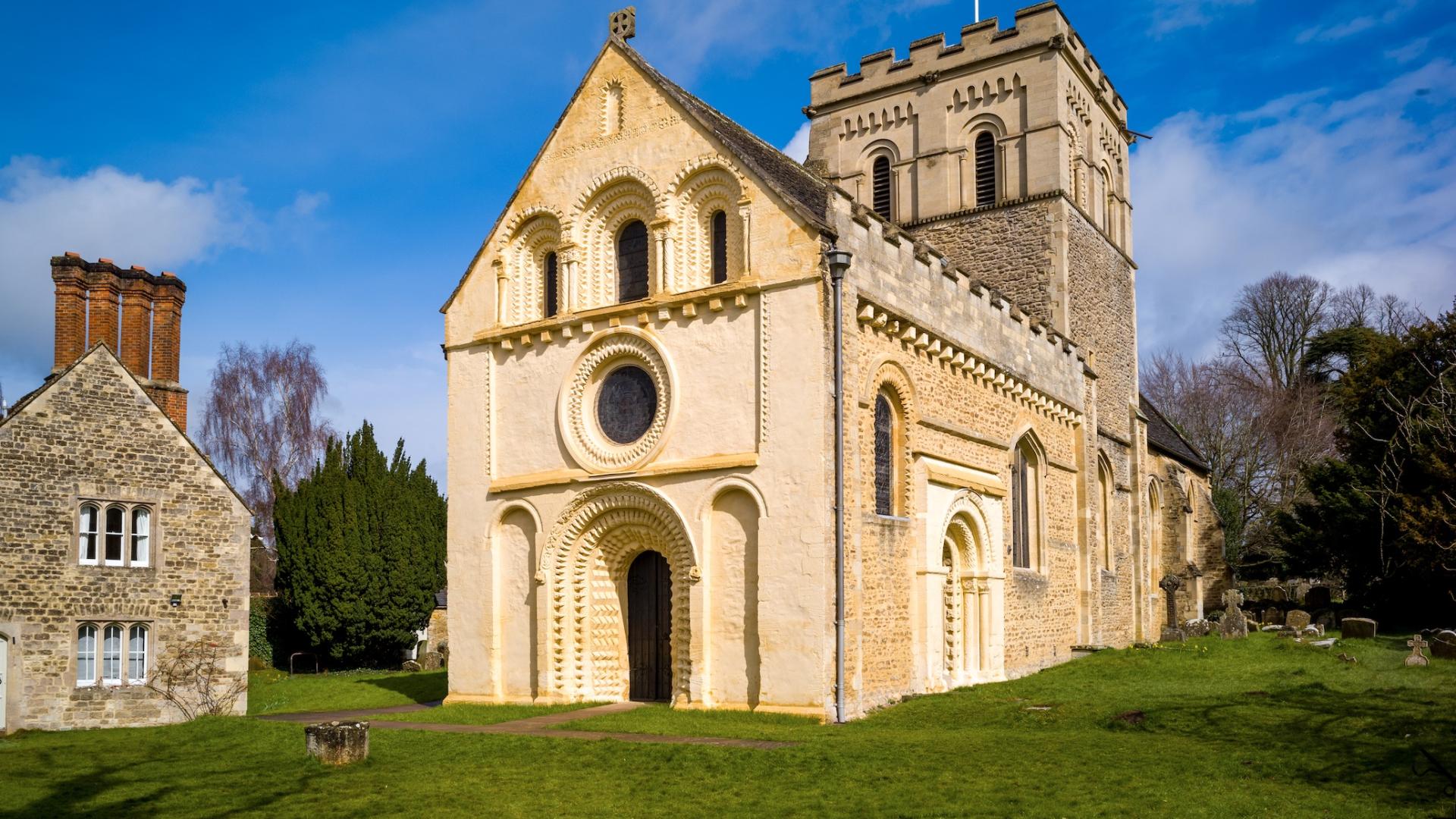 A 12th-century church with carved stone arches in a grassy churchyard.