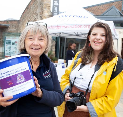 Two people standing next to each other, the left person holding up a donation bucket