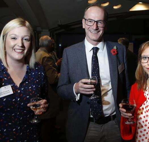 Three people standing, holding a glass of wine at the OPT awards