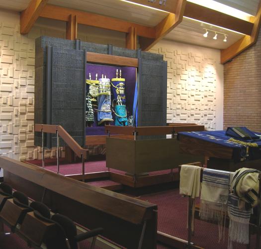 A photograph of the interior of a synagogue with a torah ark, cream walls and a purple carpet.
