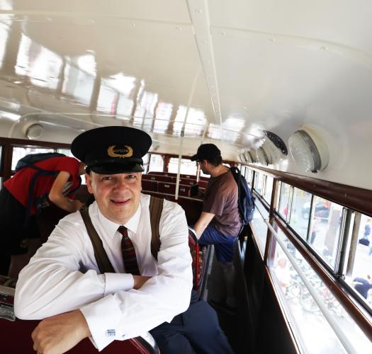A man wearing a hat that says inspector looks at the camera inside a vintage bus with a white ceiling.