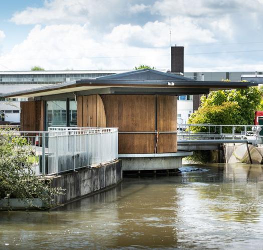Photo of a low wood-panelled building constructed over a canal.