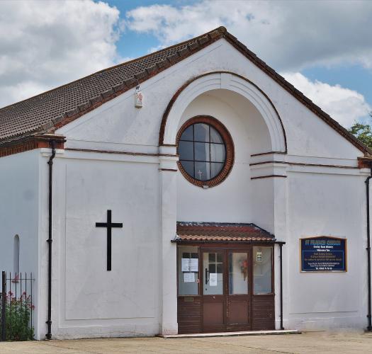 A picture of a white single-storey church building with a circular front window and a brown roof.