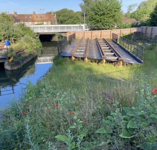 A section of moveable railway bridge in a green area next to a channel of water.