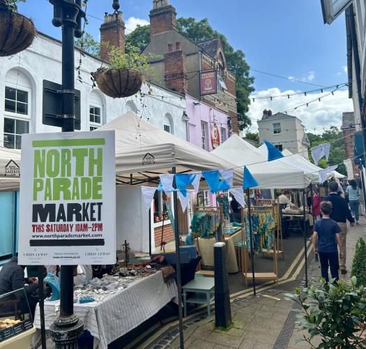 Photo of a street with market stalls covered by white marquees and a lamppost sign reading North Parade Market.