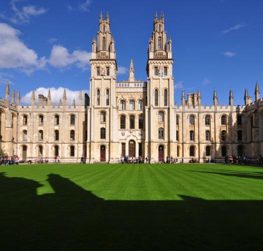 A pale stone building with towers and pinnacles set around a green lawn on a sunny day.