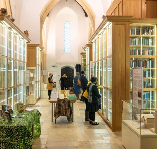 Visitors look up in a brightly lit church interior converted into archive storage with tall glass cases full of books.