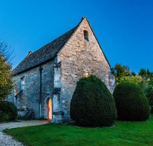 A stone chapel building lit from within in a garden at dusk.
