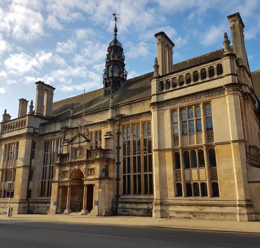 A large building made of sand-coloured stone with large windows, multiple chimneys and an ornate porch.