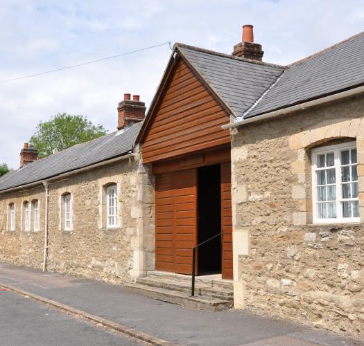 A stone building with a wooden gabled door facing a tarmacked street.