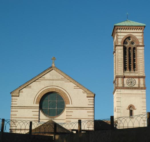 A white and red brick church building with a central circular window and a tower with a green roof to its right.