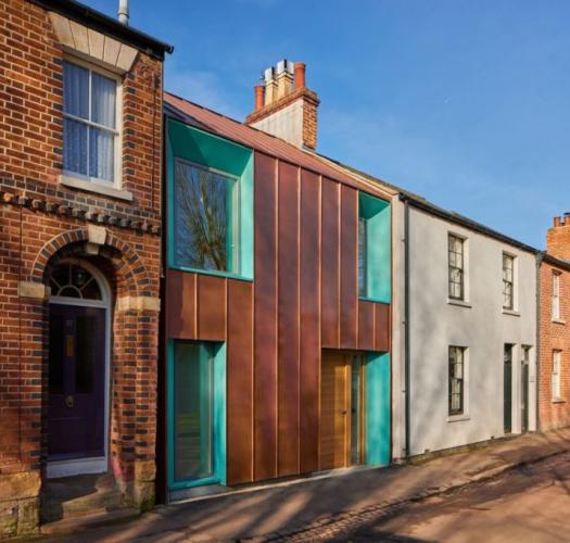 A terraced row of brick Victorian houses, with a modern building in the centre, with green copper-framed windows and rust-coloured metal cladding. 