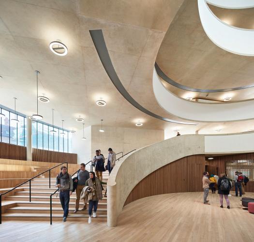The interior of a modern curved concrete building with a curved staircase and wooden floor.