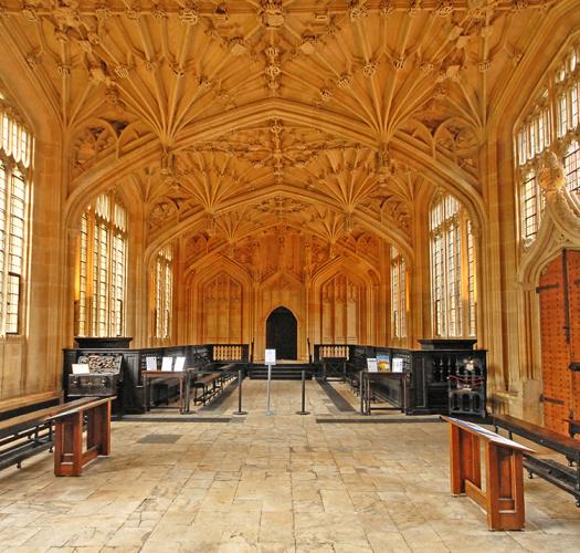 A room with an elaborate fan vaulted ceiling and wooden benches on either side.