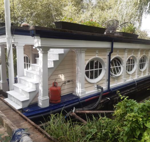 An Edwardian barge with oval windows, pilasters and a flight of steps leading up to a flat roof.