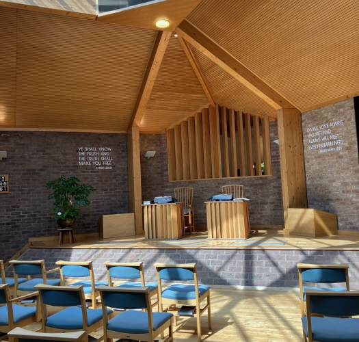 A modern church building with blue chairs laid out towards a stage with a wooden canopy.