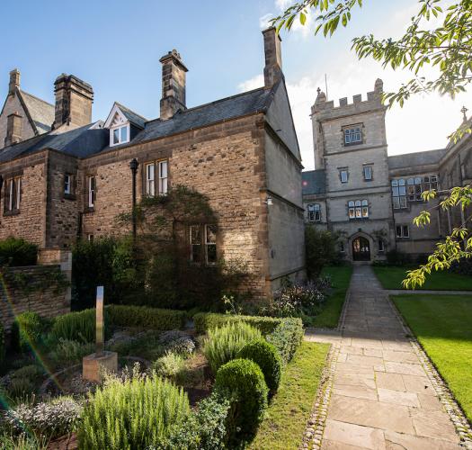 A long path through a formal garden leading to a stone building with gatetower.