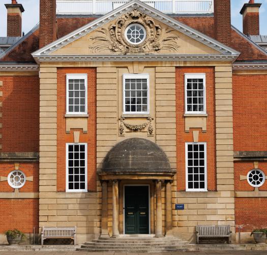 The central part of an orange brick building with pediment containing a circular window, an open cupola, and a domed ground floor doorway.