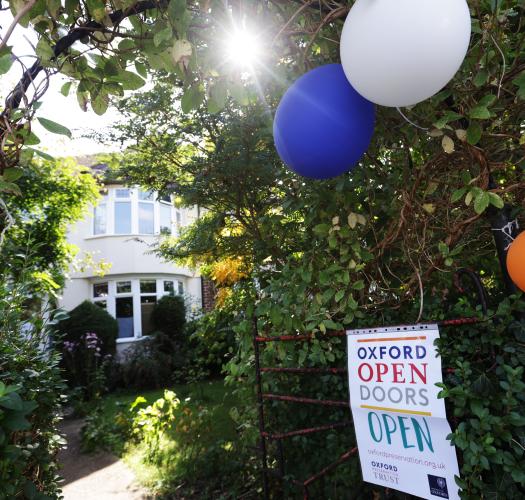 A leafy driveway leading up to a domestic house, with balloons and an Oxford Open Doors poster.