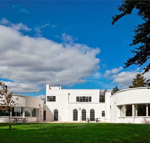 A white 1930s building with green lawns in front and blue skies behind.
