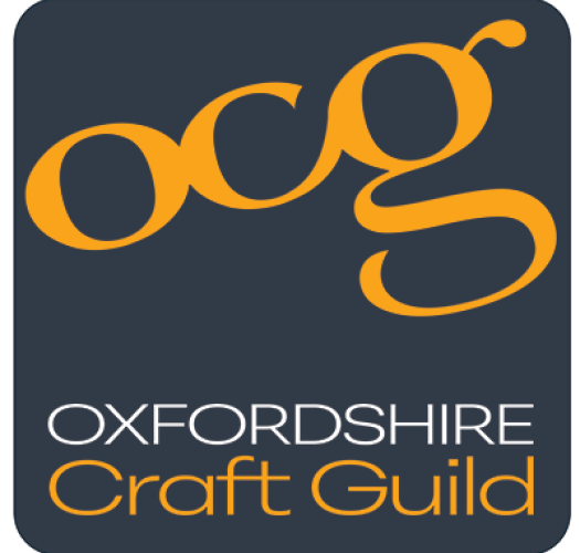 A square grey logo with a yellow title reading O C G, Oxfordshire Craft Guild.