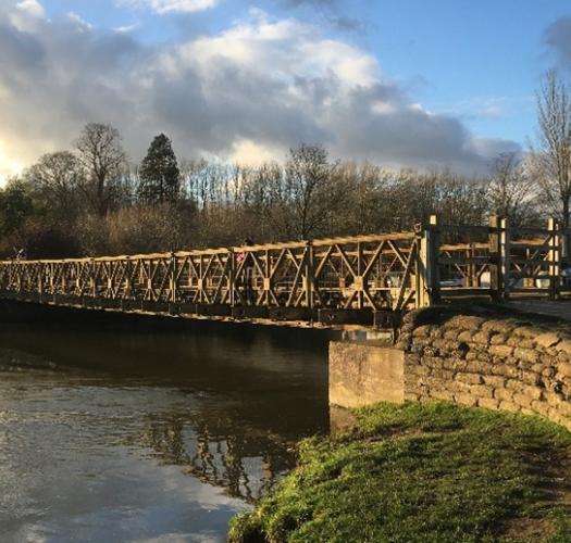 A Bailey Bridge over a river in the late afternoon sun.
