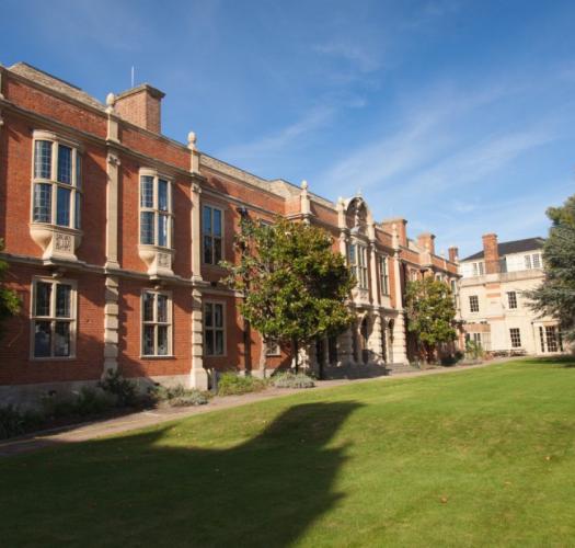 A red brick library building with stone bay windows and a large lawn in front.