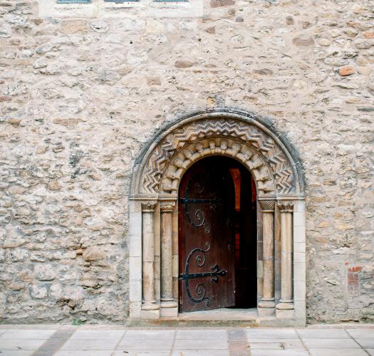 A Norman rounded doorway into a stone church with arched windows above.
