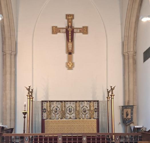 A church interior with a red carpeted altar area and a large crucifix suspended above.