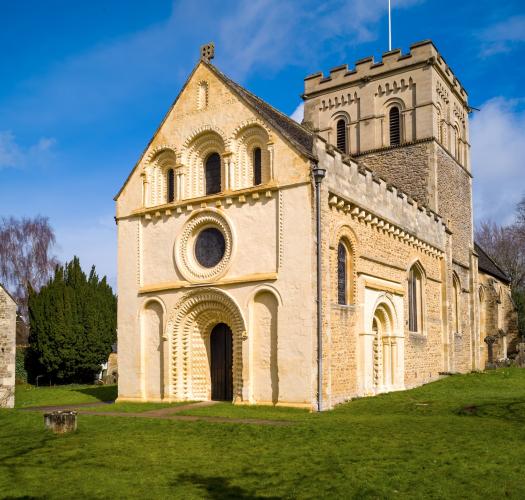 A 12th-century church with carved stone arches in a grassy churchyard.