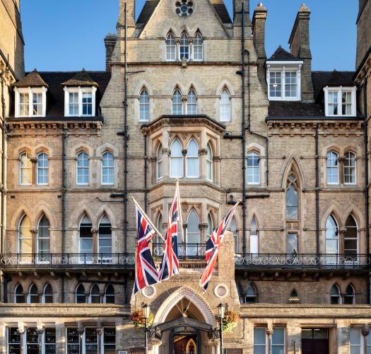 A very large Victorian brick building with three union jacks flying outside an arch doorway.