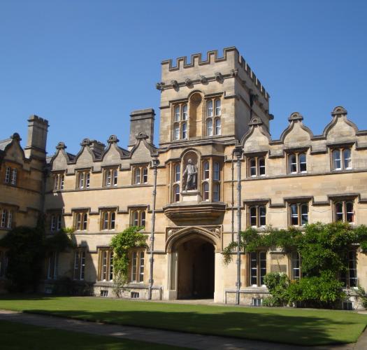 A grassy quadrangle surrounded by large stone buildings including a gatehouse.