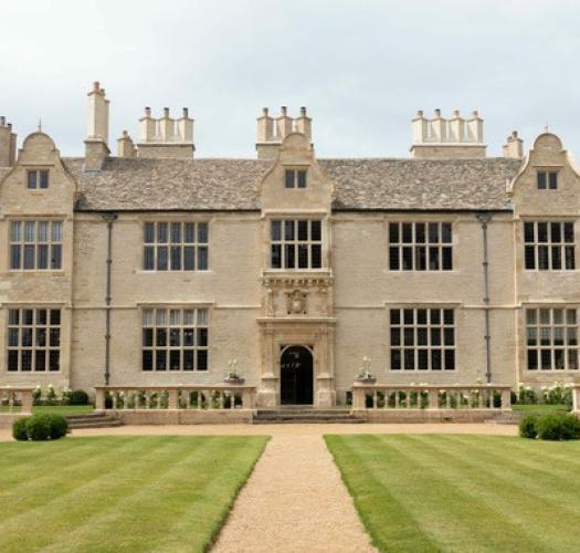 The facade of a seventeenth-century stone built manor house with large symmetrical windows, three dormers and an ornate carved entrance way.