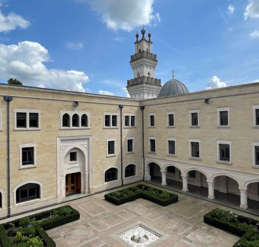 A cream-coloured buildings around a courtyard, with a minaret in the background.