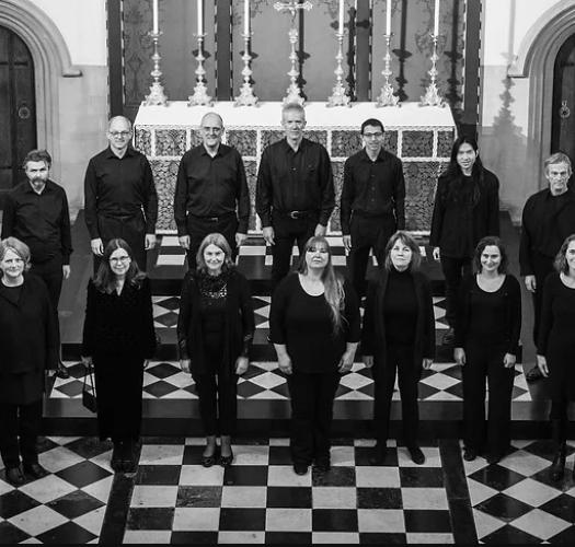A black and white photograph of a 21-person chamber choir standing in a church with a black and white tiled floor.