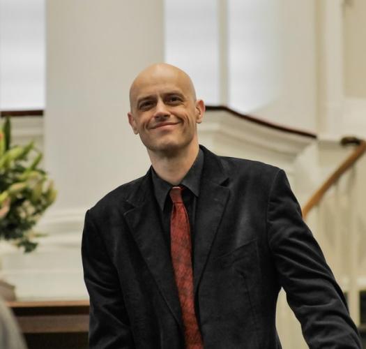 A man stands in front of a staircase wearing a jacket and tie.