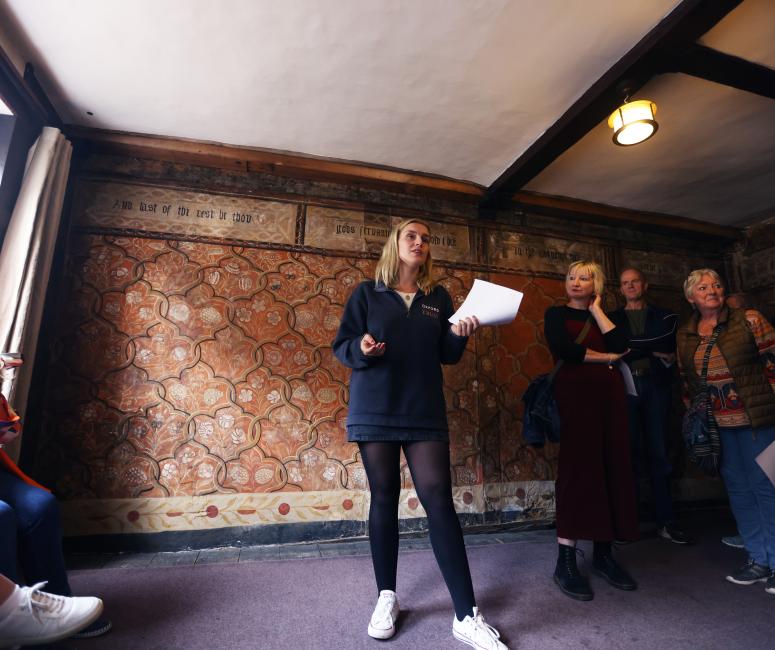 A woman standing in the painted room with a sheet of paper in her hand, talking to visitors.