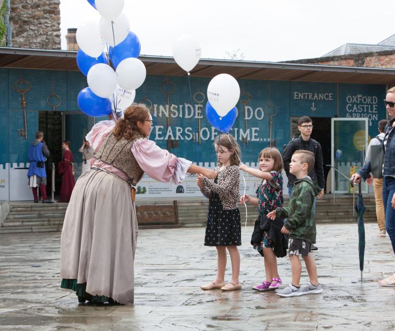 A woman handing balloons to young children at Oxford Castle