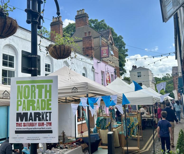 Photo of a street with market stalls covered by white marquees and a lamppost sign reading North Parade Market.