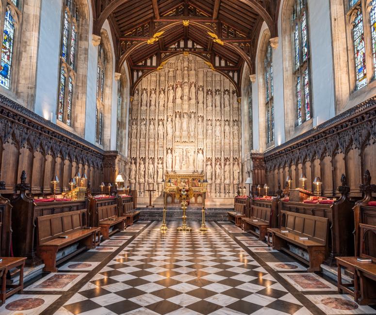 The interior of a chapel with a stone reredos, timber roof, and black and white chequered floor. 