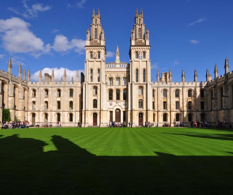 A pale stone building with towers and pinnacles set around a green lawn on a sunny day.
