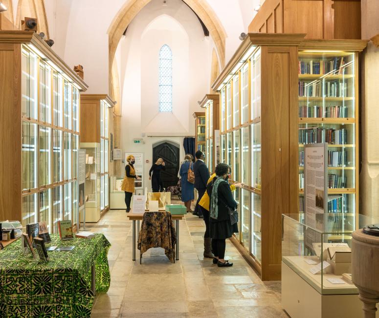 Visitors look up in a brightly lit church interior converted into archive storage with tall glass cases full of books.