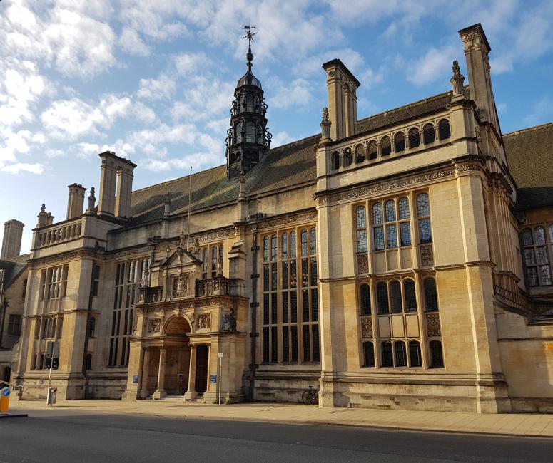 A large building made of sand-coloured stone with large windows, multiple chimneys and an ornate porch.