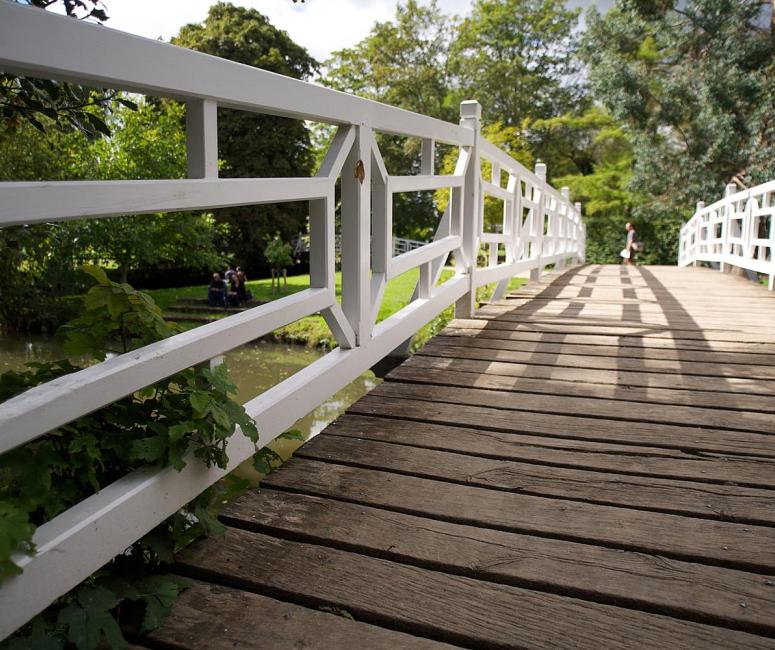 A wooden bridge in a leafy garden with white rails.