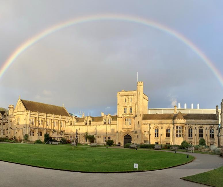 A rainbow appears over an Oxford college building with a stone gatehouse set around a circular lawn.