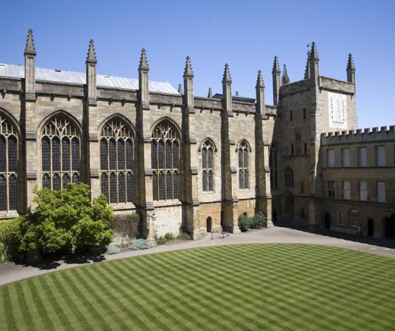 A stone chapel building with large windows and pinnacles, set around a oval lawn and against a bright blue sky.
