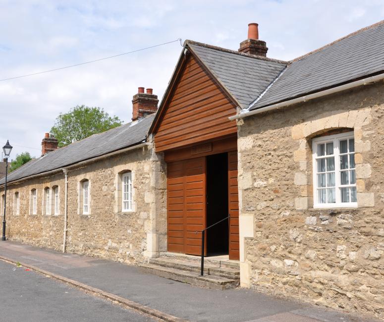 A stone building with a wooden gabled door facing a tarmacked street.